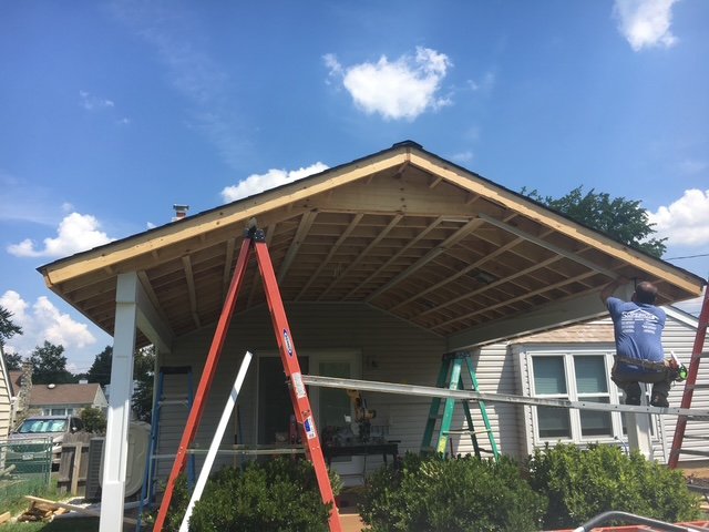 Person working on a house extension with a pitched roof, using ladders and scaffolding on a sunny day.