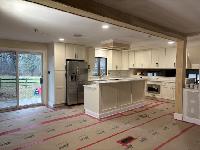 Empty kitchen with white cabinets, stainless steel refrigerator, and a sliding glass door leading outside, with construction floor protection.