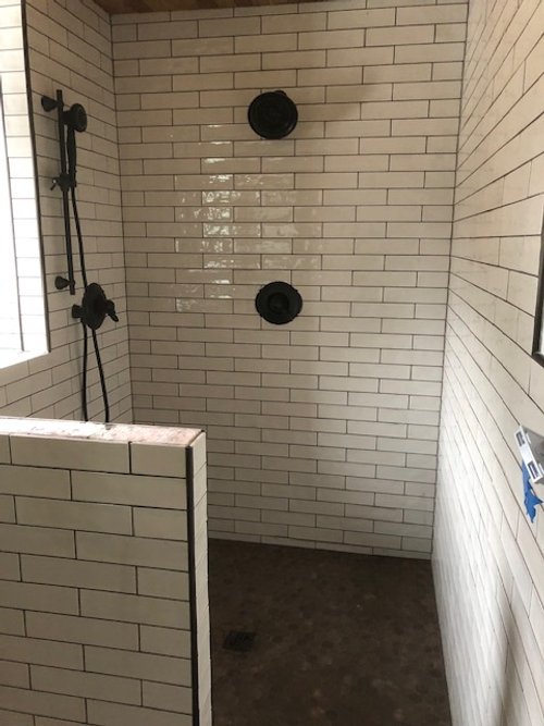Showers with white subway tile walls and black fixtures, including two shower heads and a handheld shower.