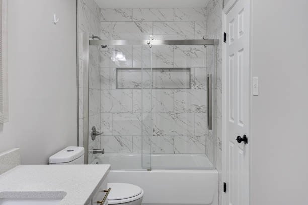Bathroom with white marble shower and glass sliding door, toilet, and white vanity with countertop.