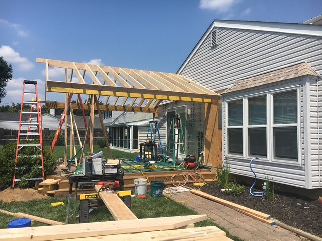 Construction of a backyard porch or sunroom extension on a house with white siding, with tools and materials scattered around.