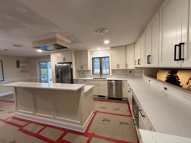 Modern kitchen with white cabinets, stainless steel appliances, and a large island with a white countertop.