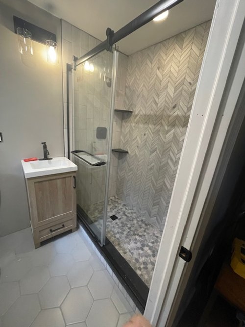 Bathroom with a small vanity sink, a glass walk-in shower with patterned tiles on the floor and wall, and built-in shelves in the shower area.