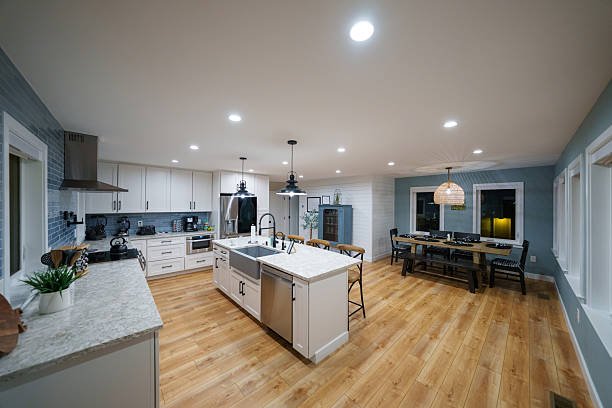 Spacious modern kitchen and dining area with white cabinets, island, stainless steel appliances, and wooden flooring.