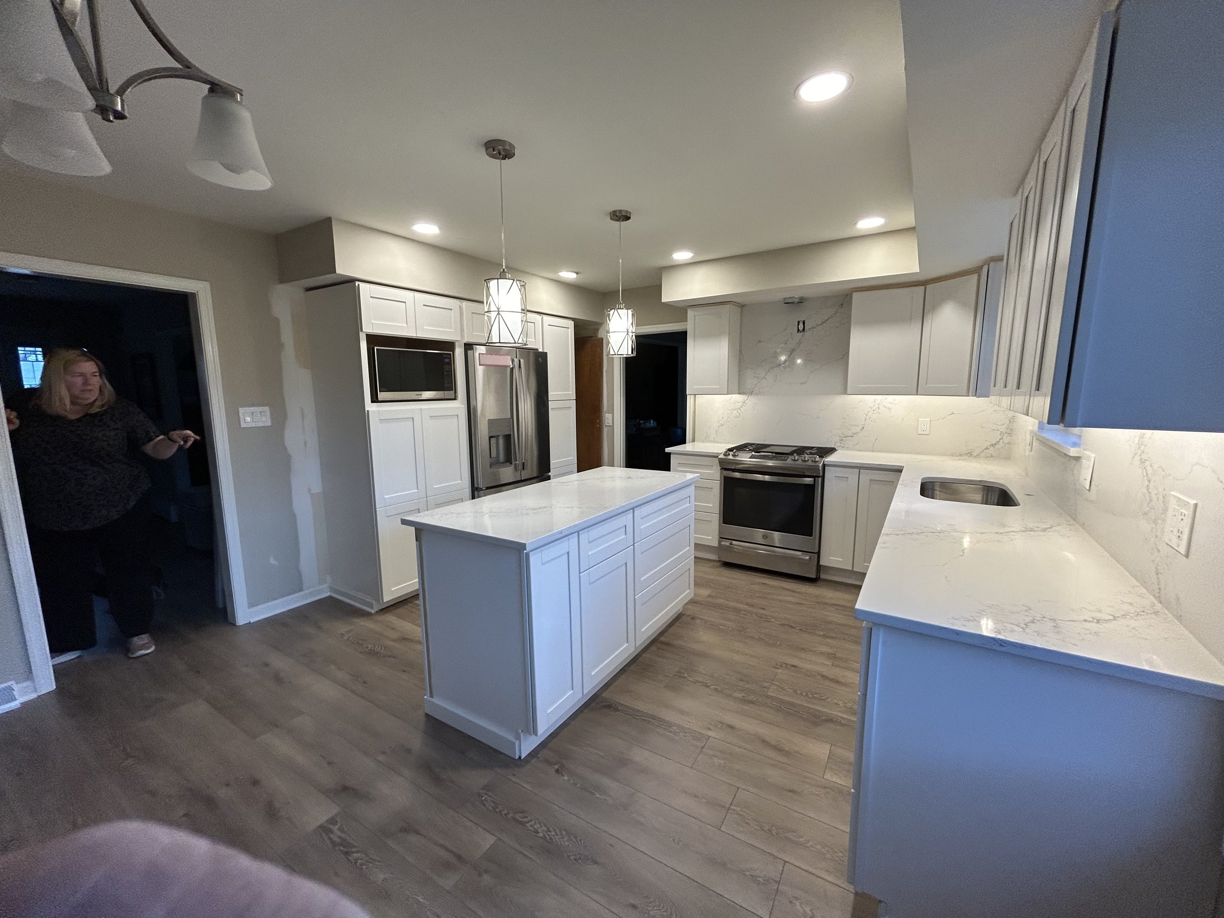 Modern kitchen with white cabinets, a central island, stainless steel appliances, marble countertops, and pendant lighting