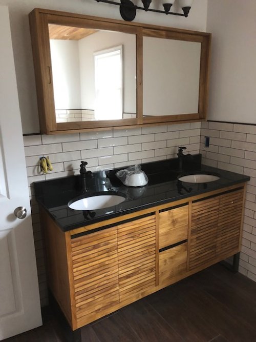 Bathroom vanity with a black countertop, two sinks, a wooden cabinet, a mirror, and light fixtures above.