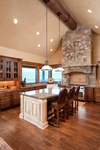 Kitchen with wooden cabinets, an island with a white base, and a stone fireplace with a large clock above it.