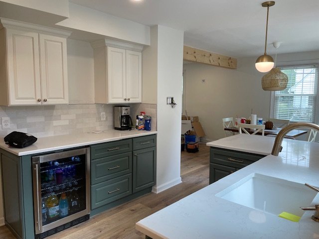 Kitchen with white and dark green cabinets, a small fridge, coffee maker, and a dining area with a white table and chairs near a window with blinds.