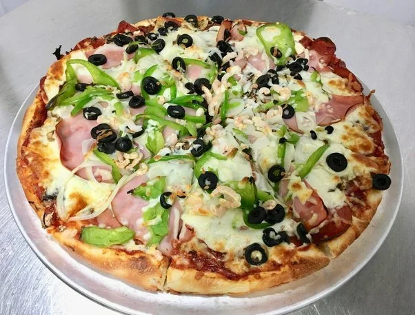 Pizza topped with green bell peppers, black olives, ham, onions, and cheese on a silver tray.