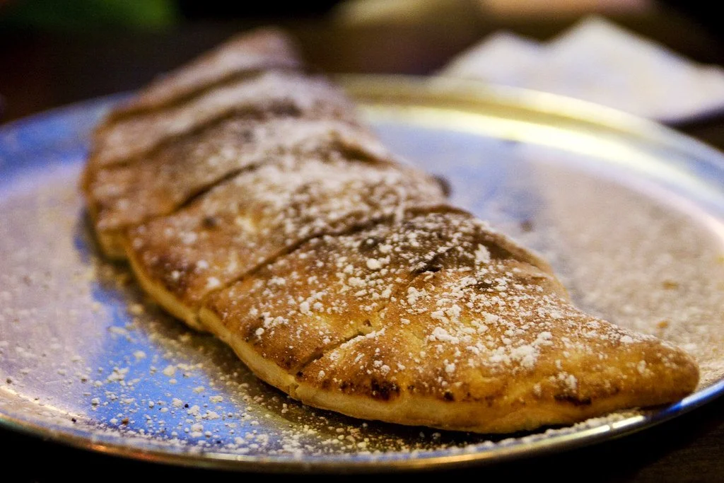Close-up of a piece of grilled flatbread topped with powdered sugar on a metallic plate.