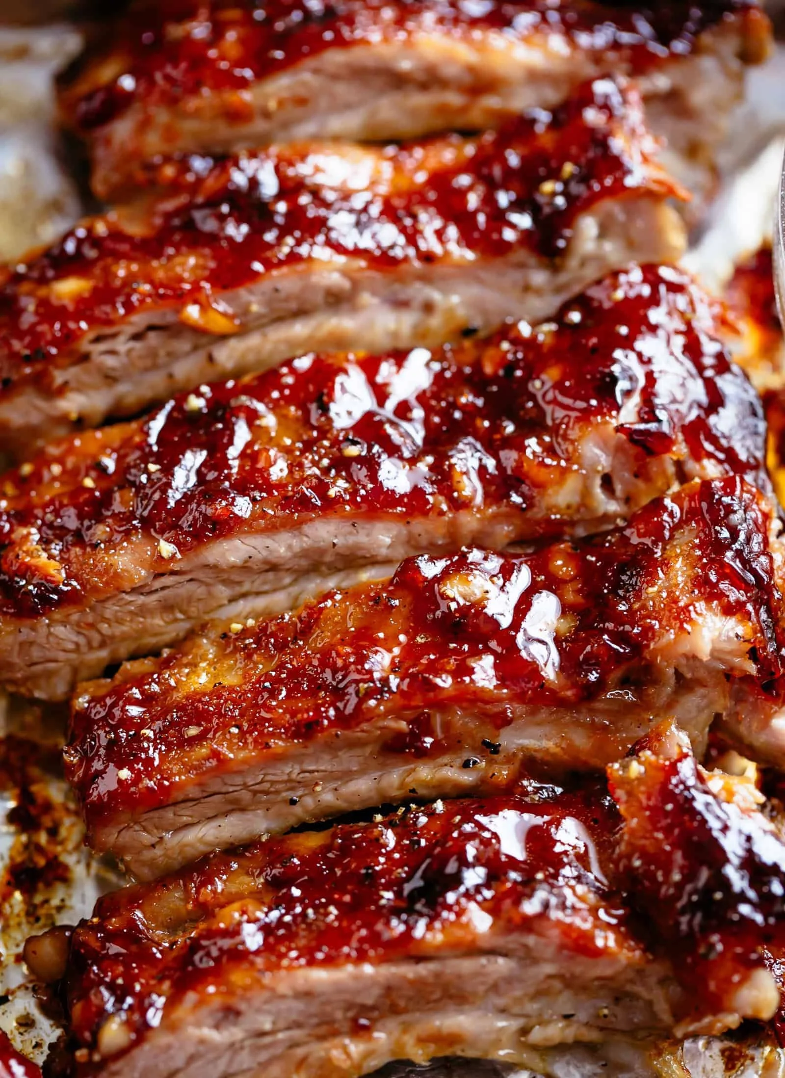 Close-up of glazed ribs, cooked and sliced, with barbecue sauce.