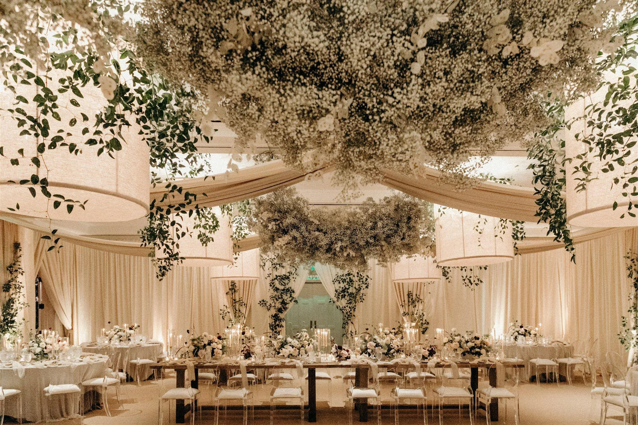 Elegant banquet hall decorated with hanging white lanterns, lush greenery, and floral arrangements for a wedding or formal event.
