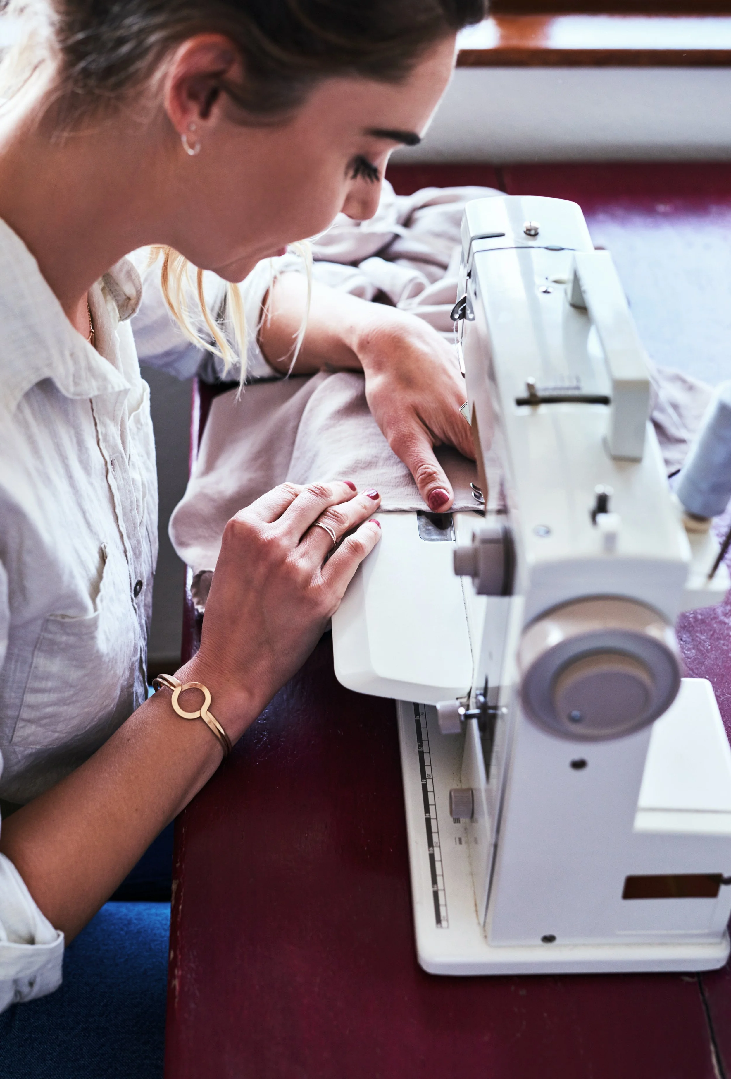 Close-up of a person guiding pale pink fabric through a sewing machine, hands steadying the seam as it feeds through.