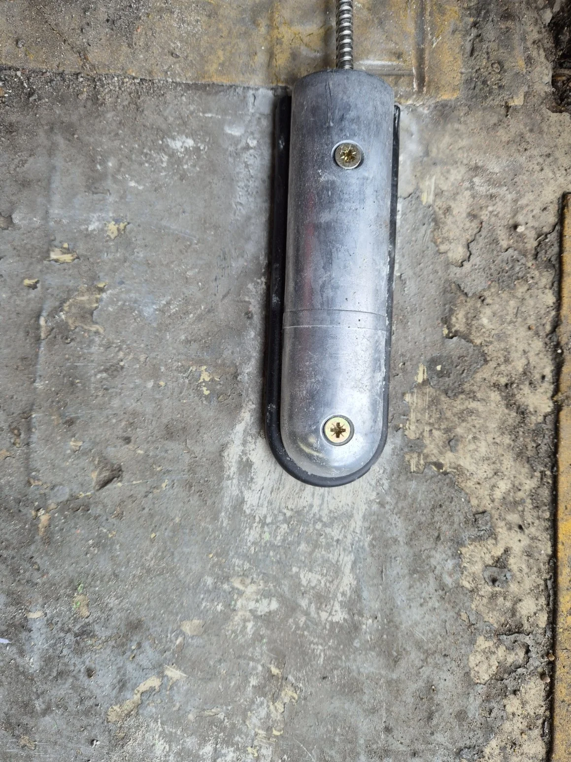 A floor spring door closer mechanism with a metal casing installed on a concrete floor near a brick wall.