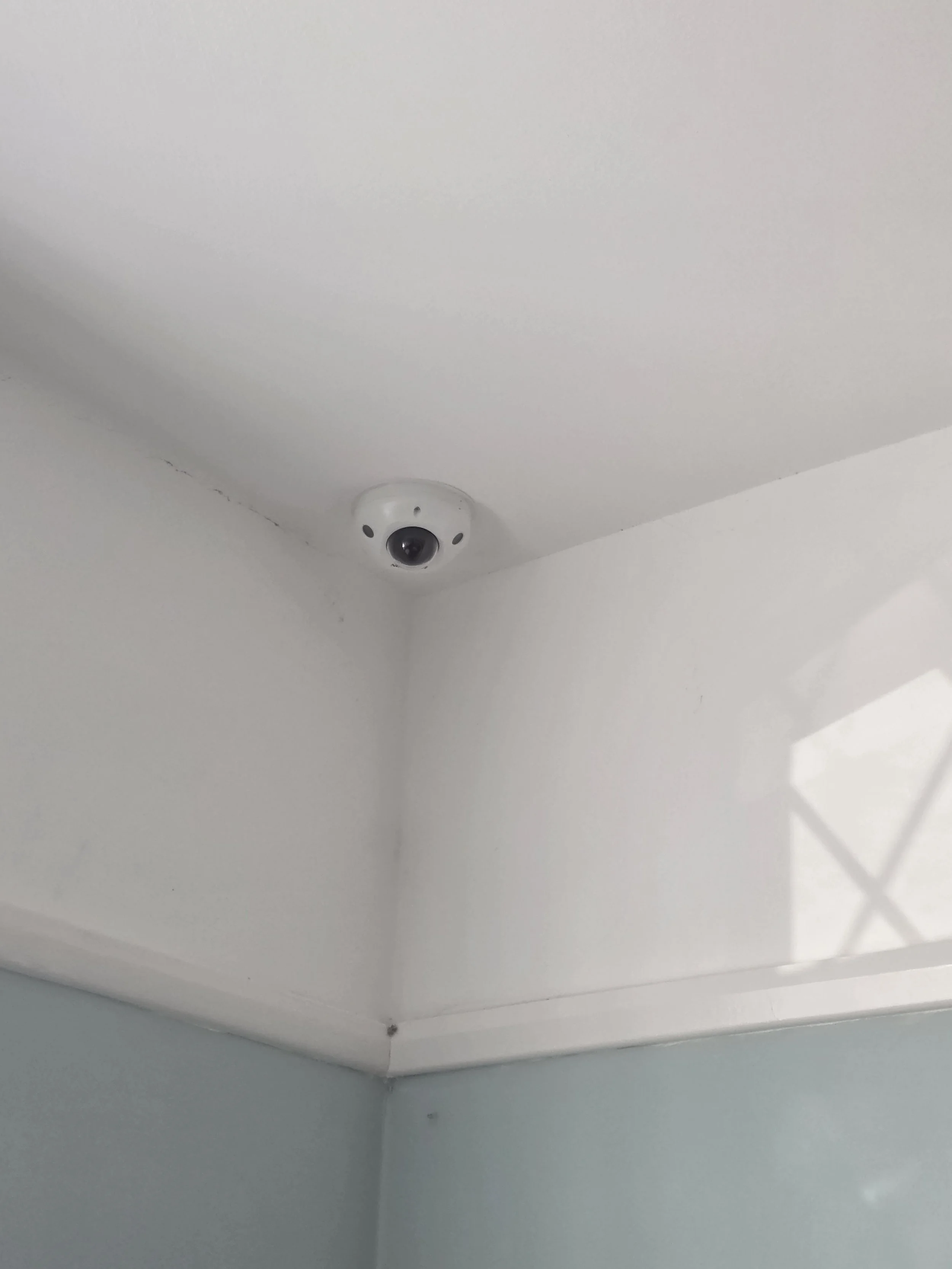 A ceiling corner with a white security camera mounted near the ceiling.