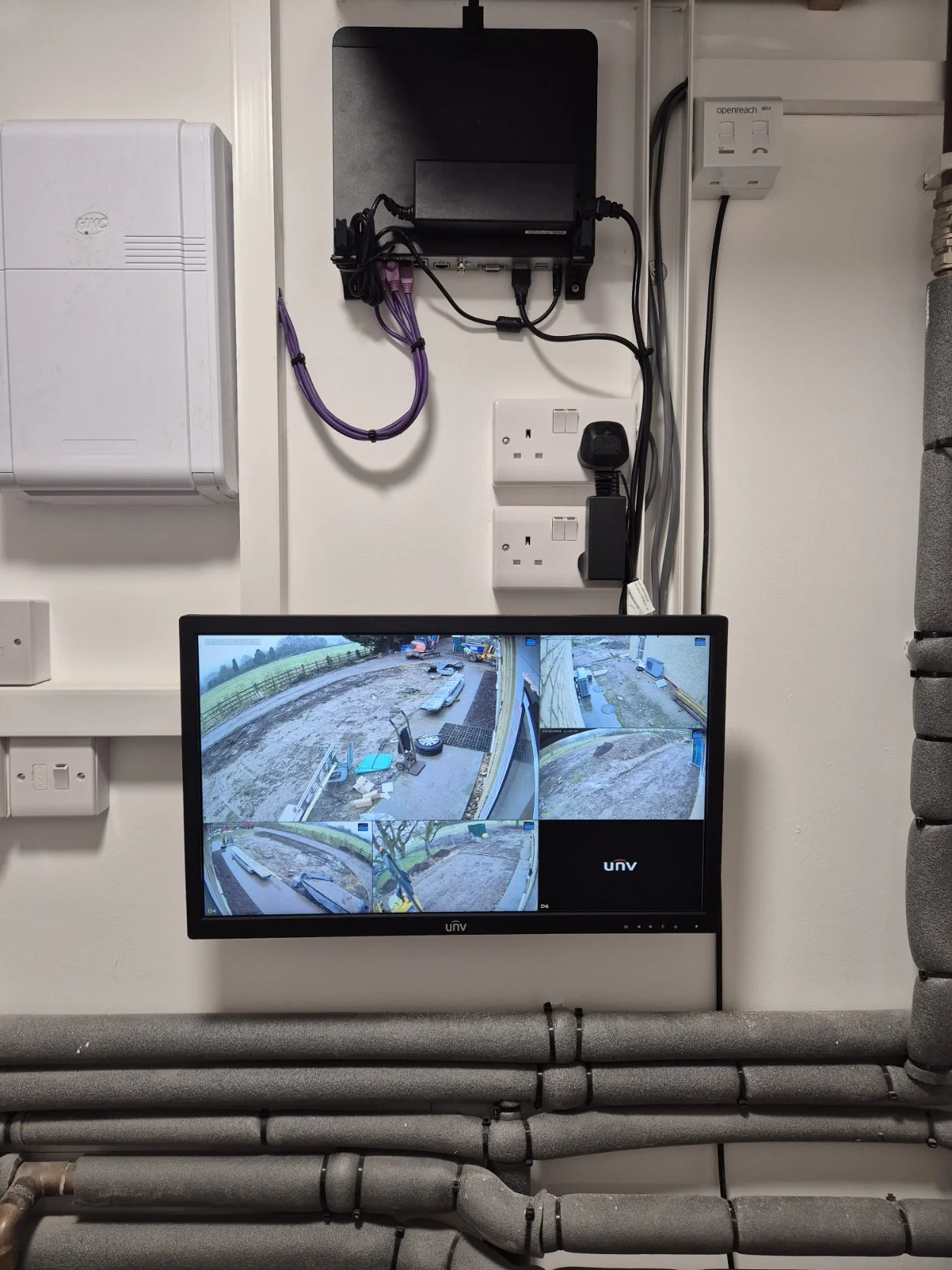 A security monitor displaying four camera feeds showing an outdoor construction site.