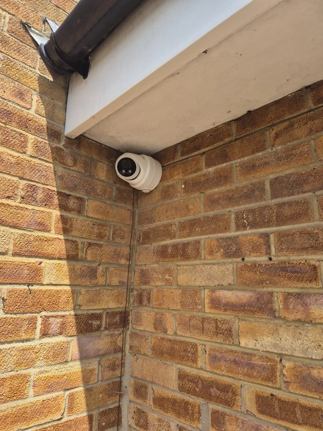 A security camera mounted in the corner of a brick exterior wall under a white sofit