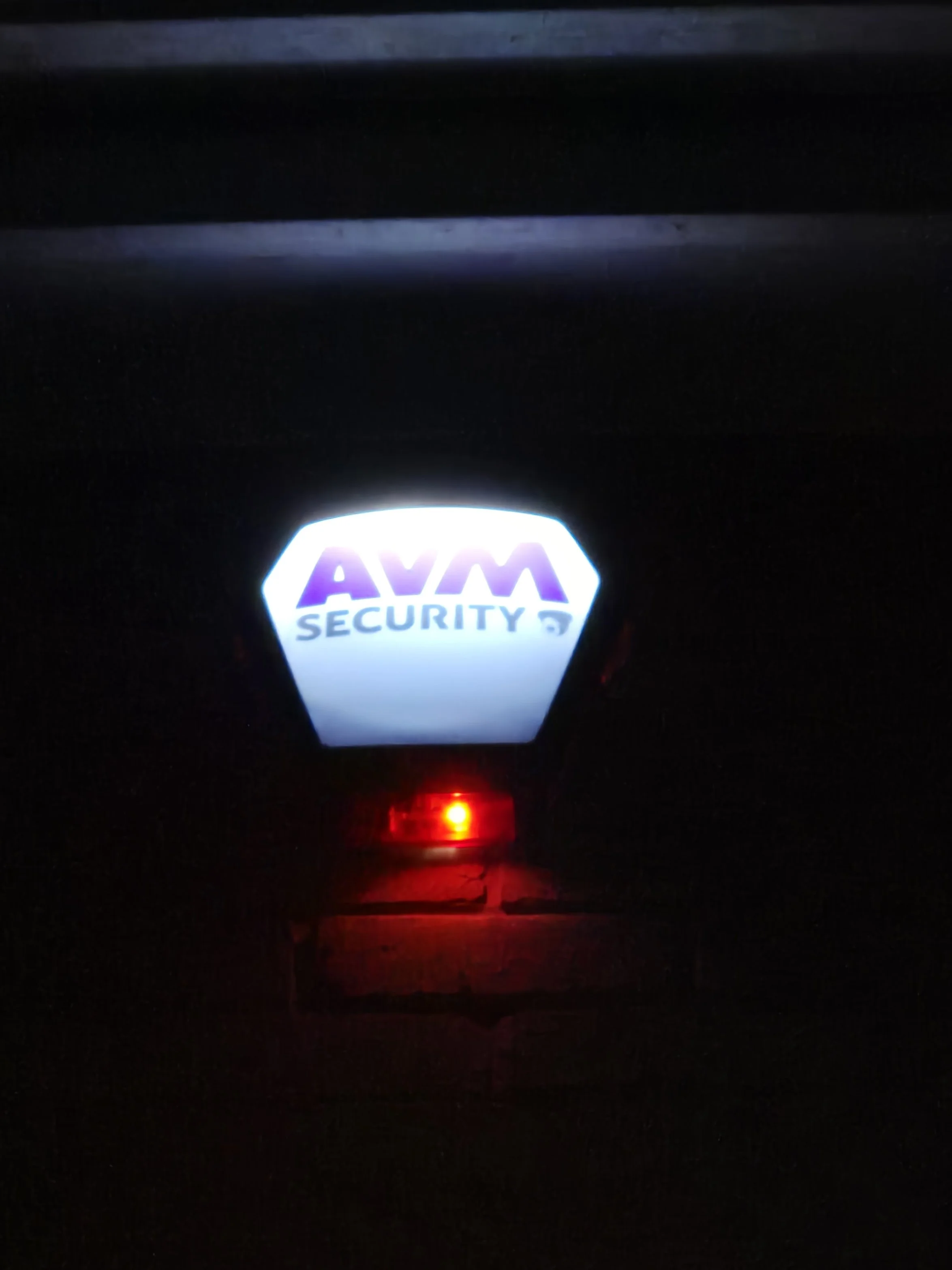 An ATM security light with the text  AVM SECURITY illuminated in purple and blue, with a red indicator light below.