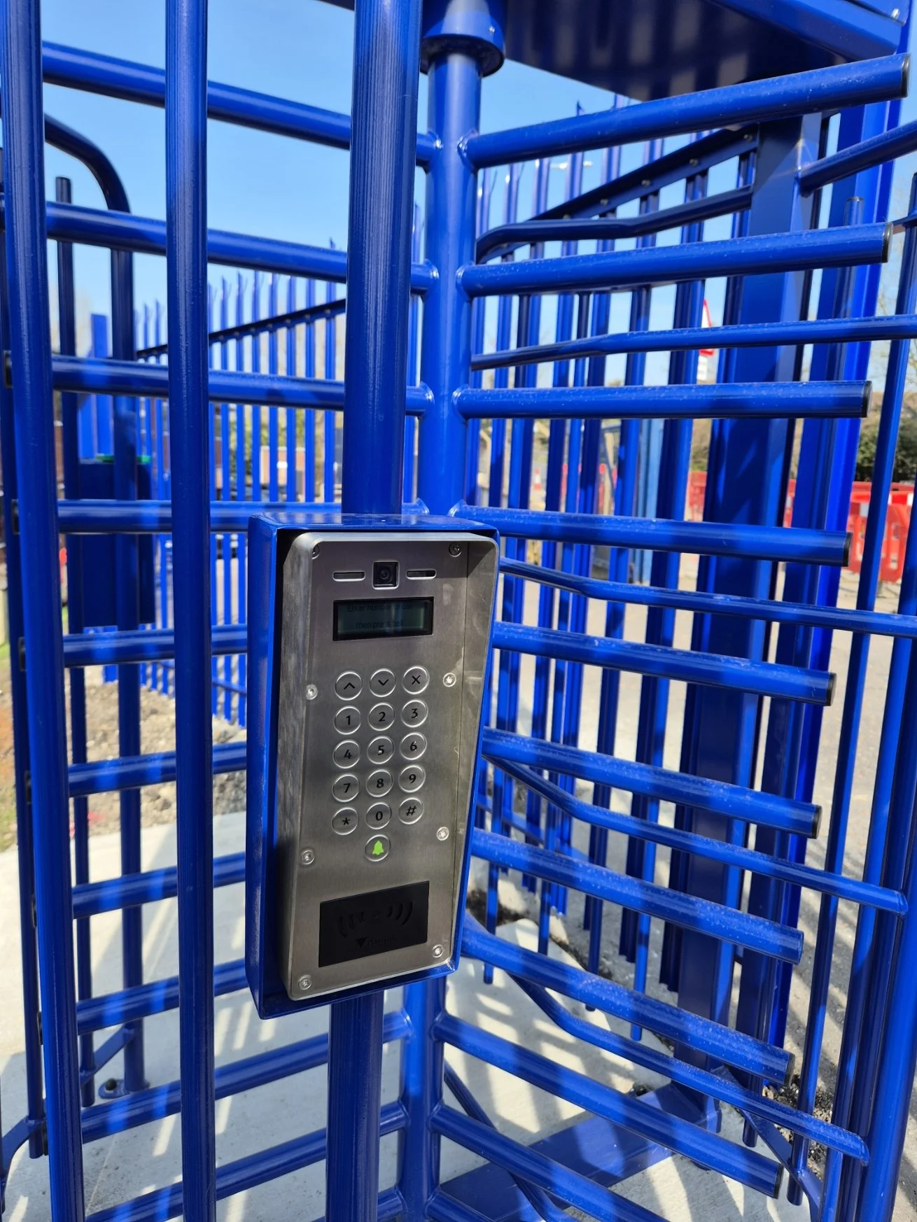 A security keypad mounted on blue metal bars at a playground entrance.