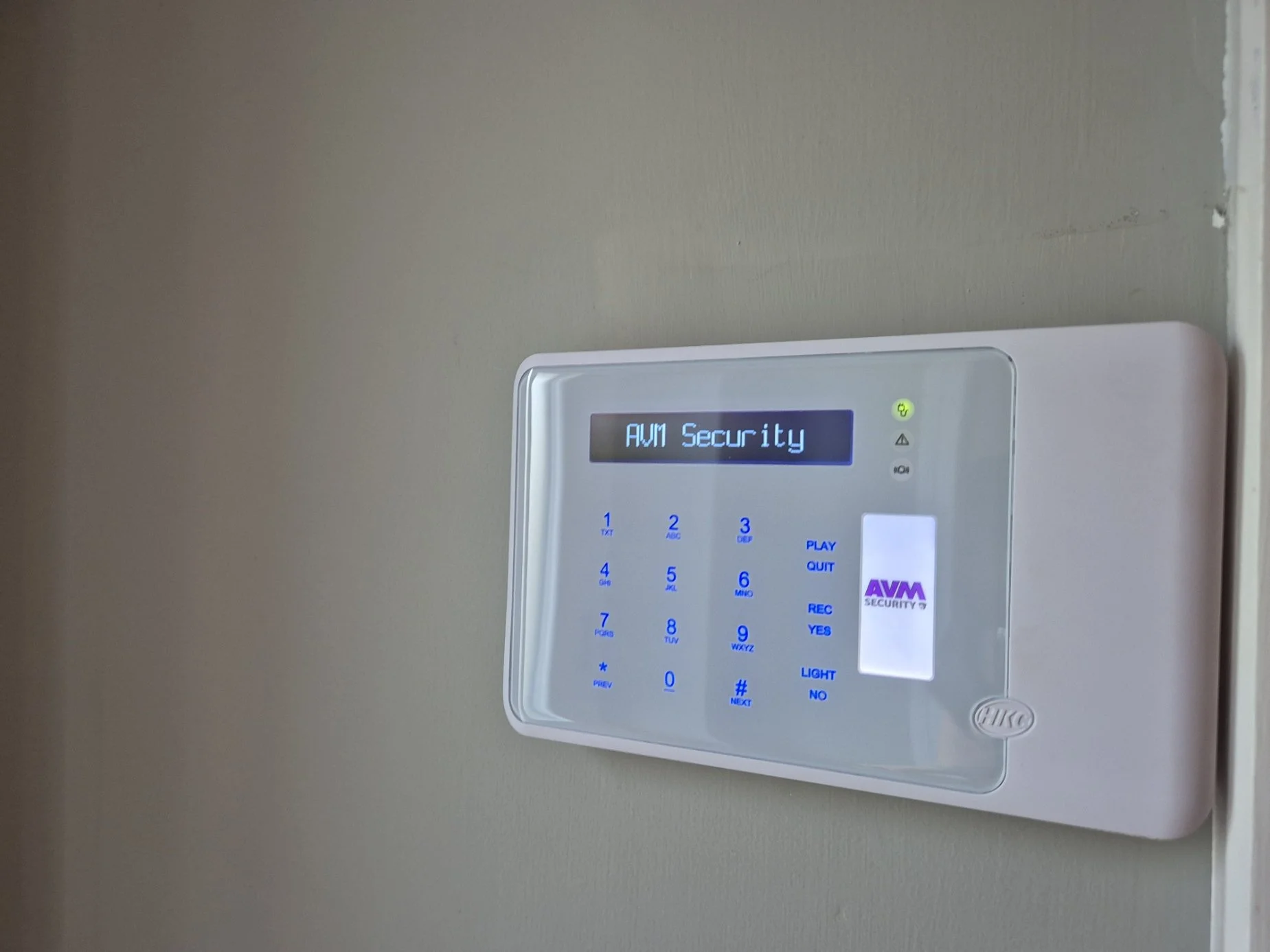 Security system control panel with a display reading 'AWM Security' and a sticker with 'AWM SECURITY' logo.