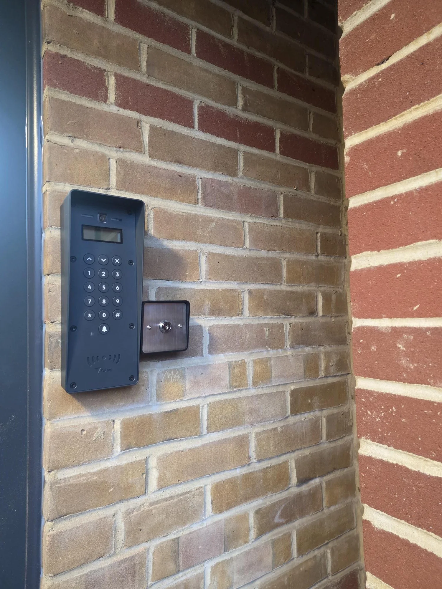 Video intercom and key card reader mounted on brick wall outside building entrance.