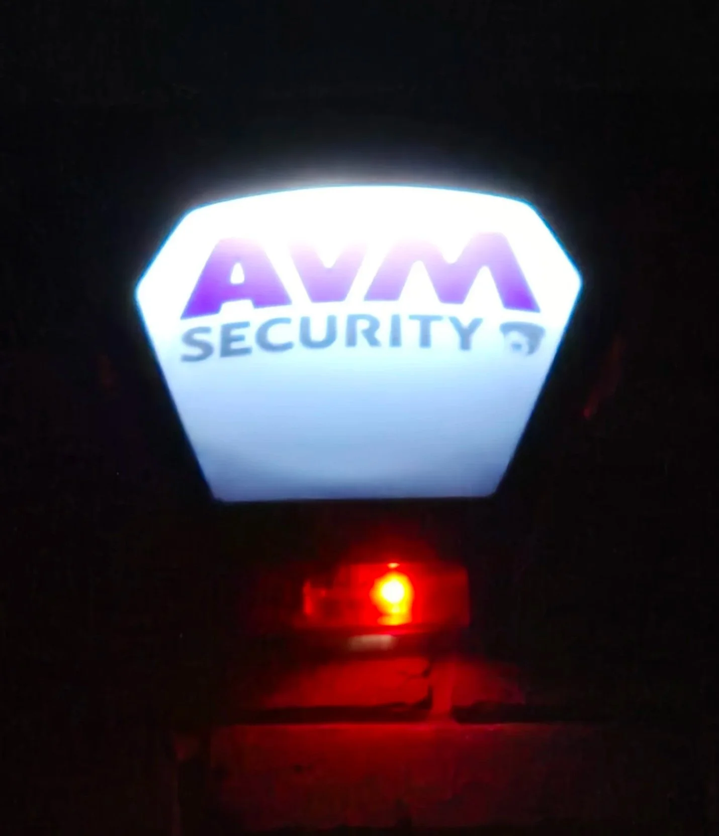 Illuminated security sign with purple and white text reading 'AVM SECURITY' in dark surroundings.