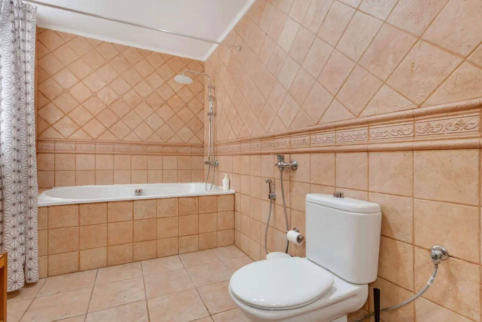 Baño con azulejos color terracota, ducha con cortina en la esquina izquierda, inodoro blanco y pipeta, en el fondo una pared inclinada y un piso de azulejo.