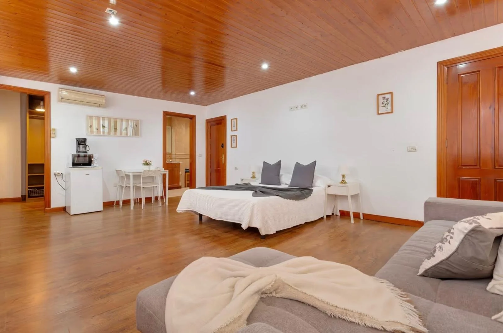 Habitación con cama, sillón y zona de cocina en madera.