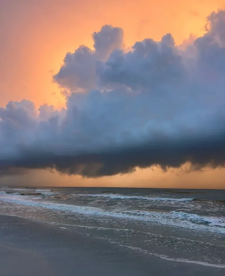 View of sunset over ocean with dark storm clouds and gentle waves, taken by Addison Allen, a Therapist for Trauma, OCD, and Faith-Based Missionaries - serving Largo, FL, Tampa, FL, Saint Petersburg, FL, and San Antonio, TX