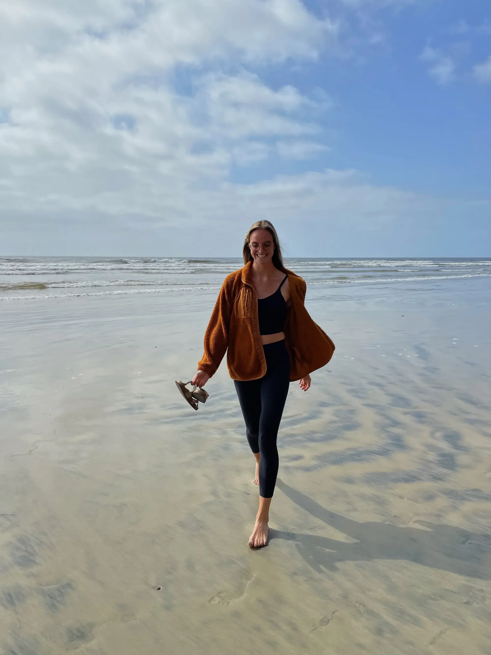 Addison Allen, trauma therapist in Largo, Florida, offering EMDR therapy and anxiety therapy, walking barefoot on the beach during a Beach Walk Therapy session with the ocean and cloudy sky in the background.