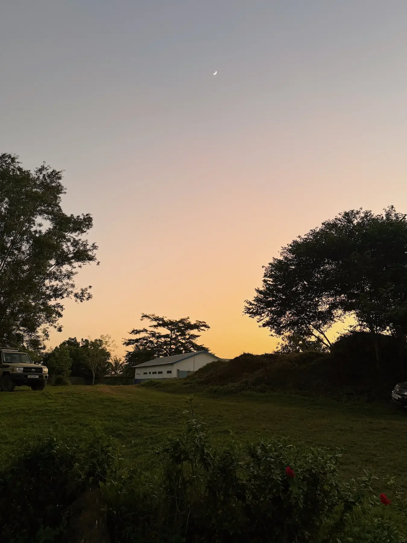 Dusk scene in rural Africa with a crescent moon, white building, and natural landscape, reflecting the global and spiritual context of Christian therapy for international missionaries with Addy Allen, trauma and anxiety therapist