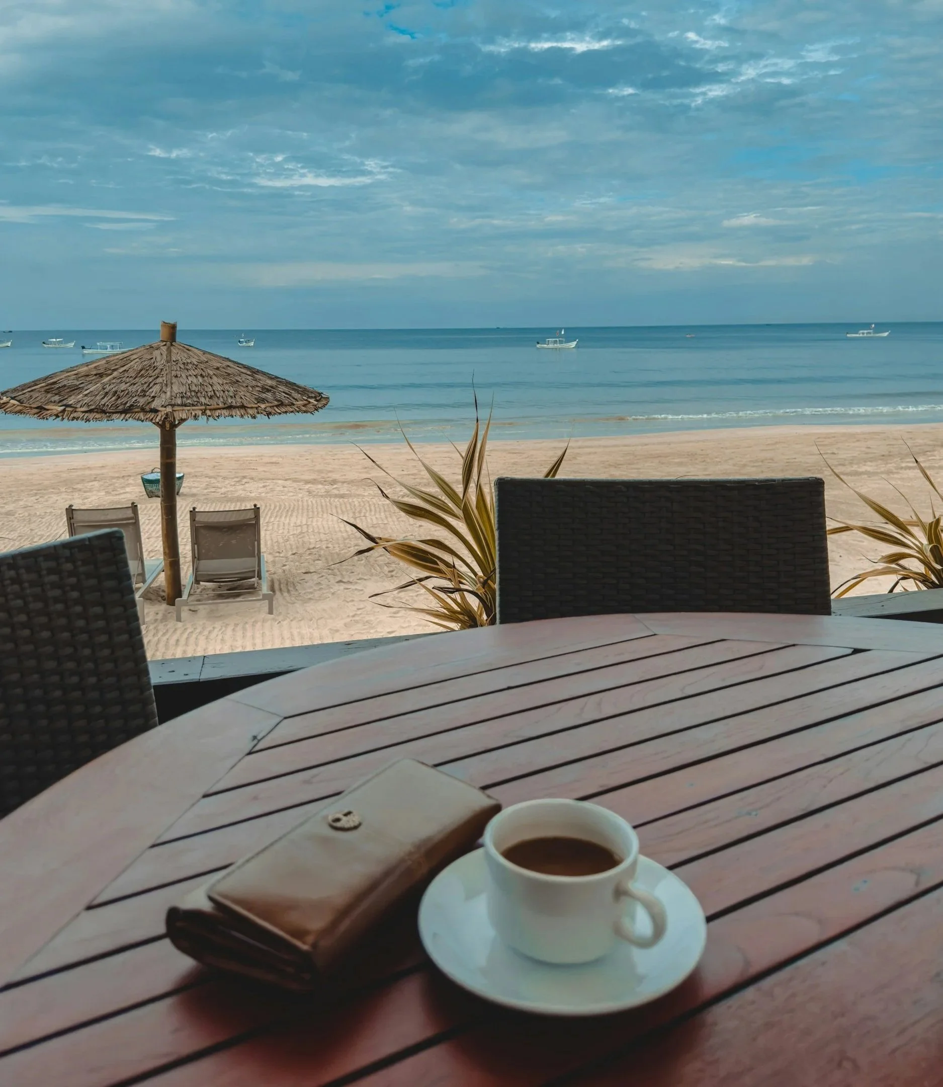 A beach scene with a wooden table set with a cup of coffee overlooking the ocean - Trauma and EMDR Therapy, OCD Therapy, Therapy for Young Adults, and Therapy for Missionaries in Texas, Florida, and Beyond