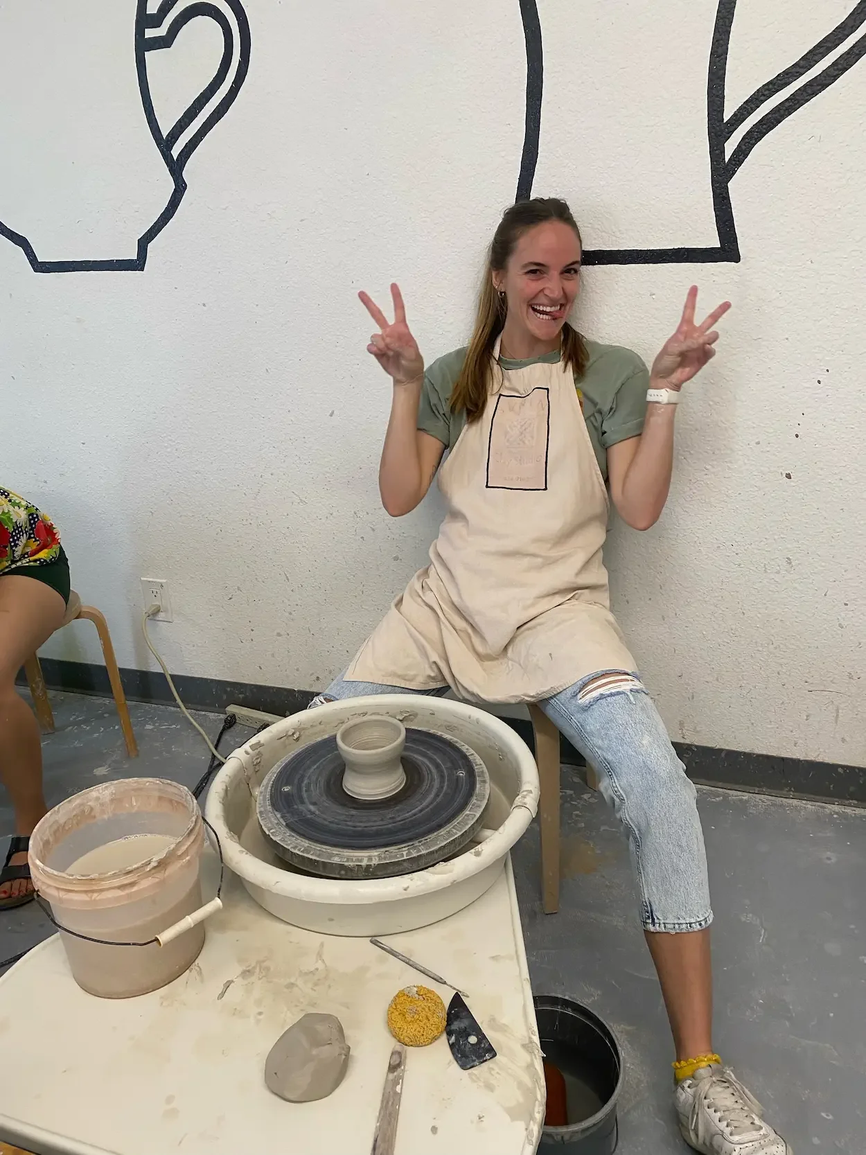 Addy Allen, therapist in Largo, Florida and San Antonio, Texas, specializing in EMDR therapy and anxiety therapy, smiling and making peace signs while sitting at a pottery wheel highlighting creative self-care for young adults in their 20s and