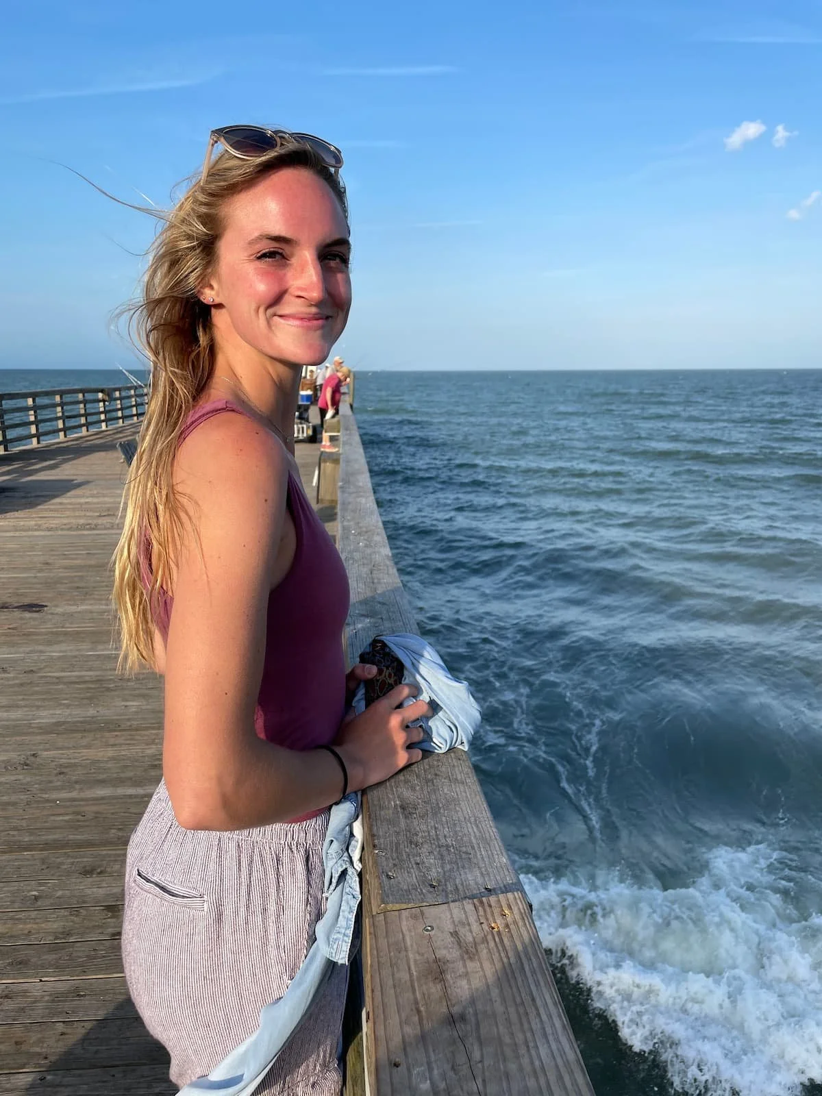 Addy Allen, trauma and anxiety therapist in Largo, Florida at Indian Rocks Beach, smiling on a wooden boardwalk by the ocean, illustrating the peaceful, grounding experience of Beach Walk Therapy.