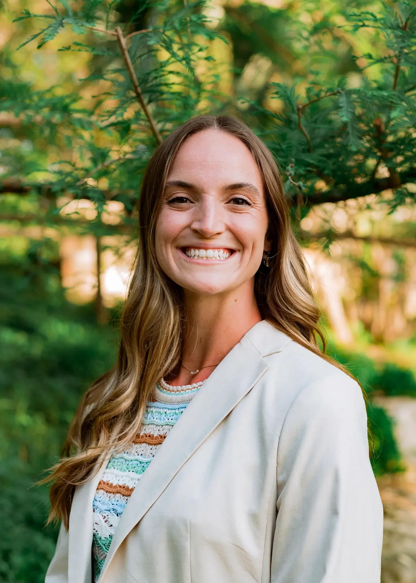 Addison Allen, licensed therapist in Largo, Florida and San Antonio, Texas, specializing in EMDR therapy, anxiety therapy, and trauma therapy, smiling outdoors in front of green trees.