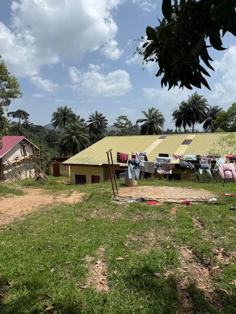 Rural scene from Africa featuring a yellow house, laundry on a clothesline, and palm trees, symbolizing cultural connection and global perspective in Christian therapy for international missionaries with Addy Allen, trauma and anxiety therapist