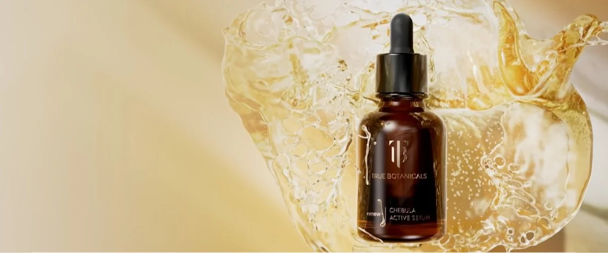 A brown glass dropper bottle labeled '11' with 'True Botanicals' and 'Chebula Active Serum' surrounded by splash of a yellowish liquid.