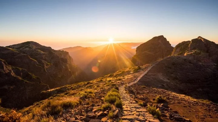 Sunset over rugged mountain landscape with a stone path.