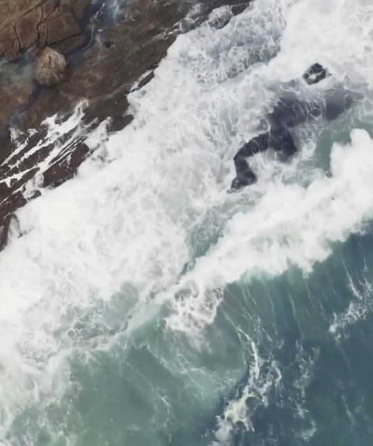 Waves crashing against rocks along a shoreline.
