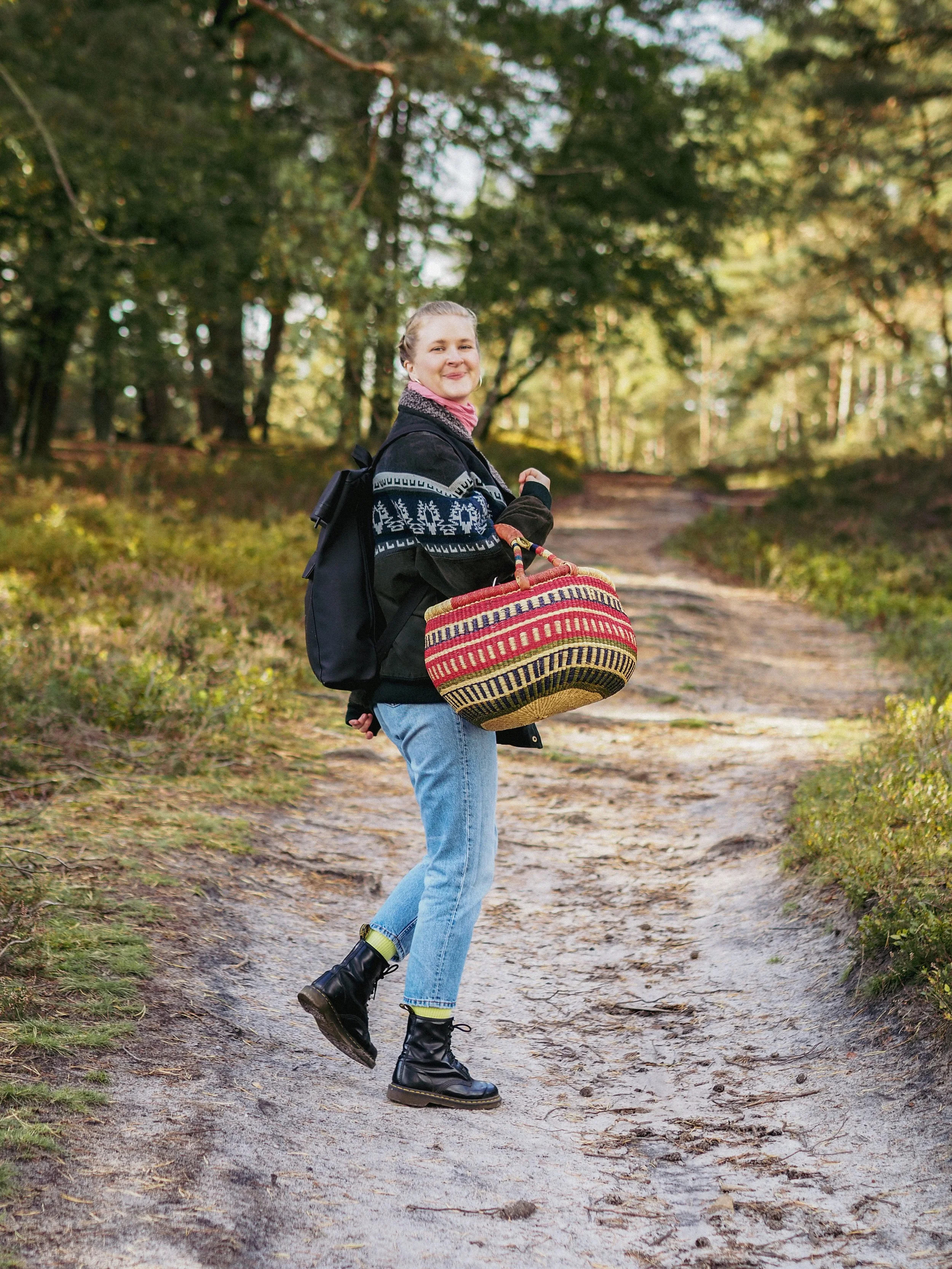 Eine junge Frau mit Rucksack und Korb im Wald auf einem Wanderweg.