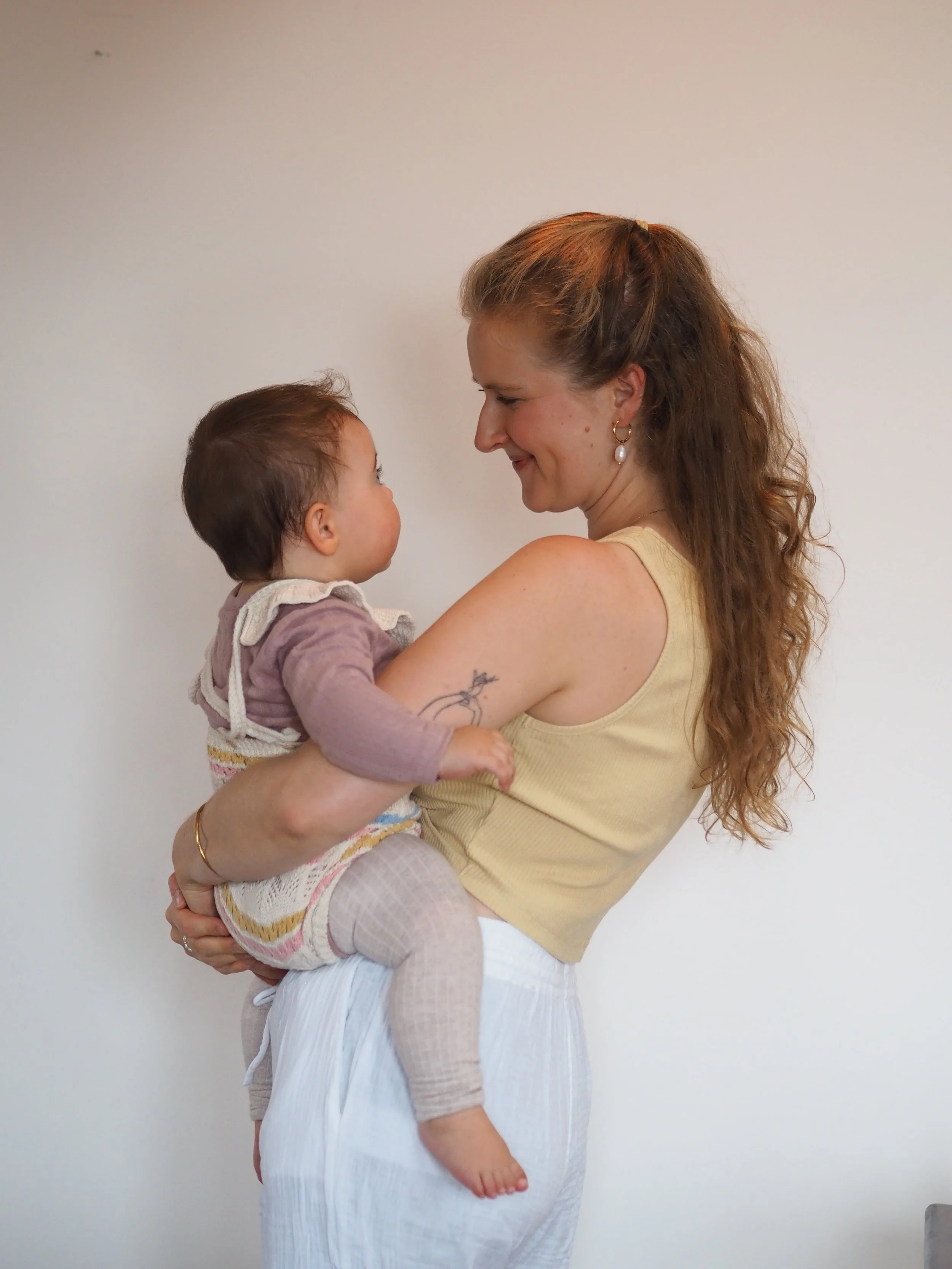 Eine Frau hält ein Baby im Arm und lächelt liebevoll.