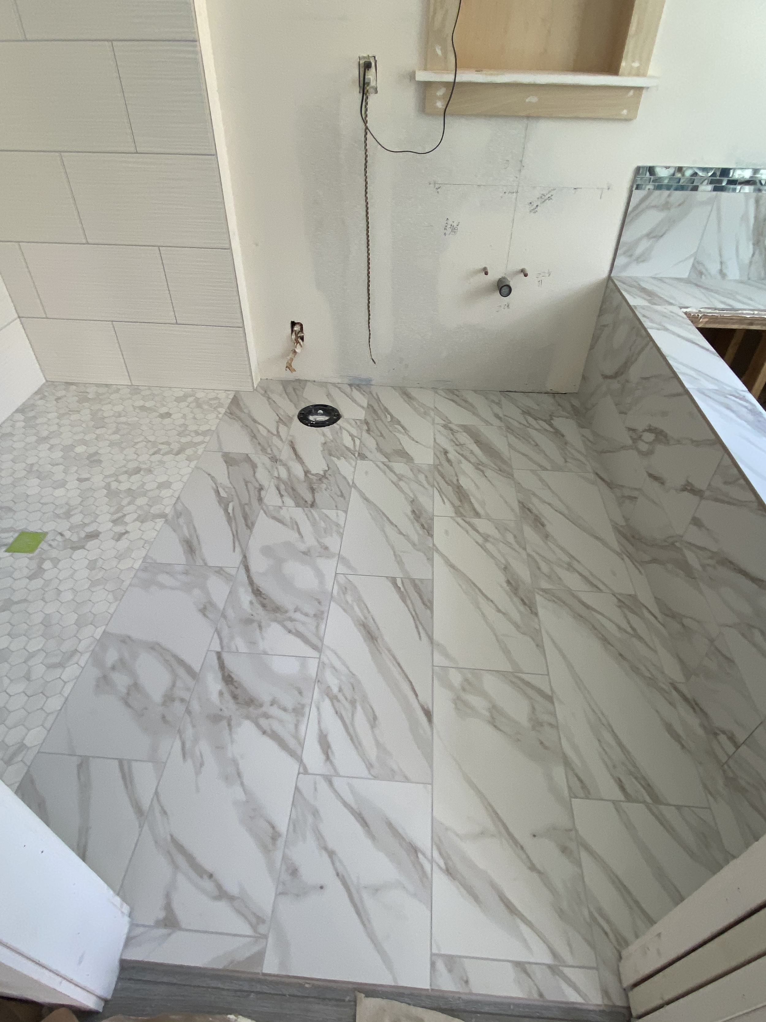 Room under construction with new marble-look tile flooring, partially tiled walls, and exposed wiring and plumbing.