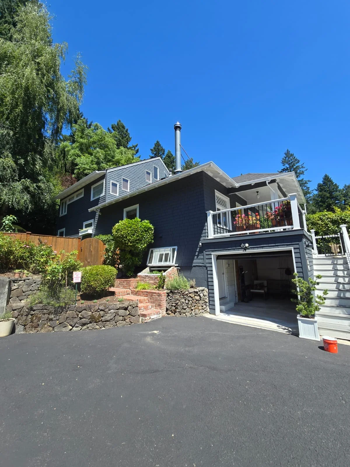 A multi-story house with a dark blue exterior, white trim, and a parking garage in a residential neighborhood under a clear blue sky.