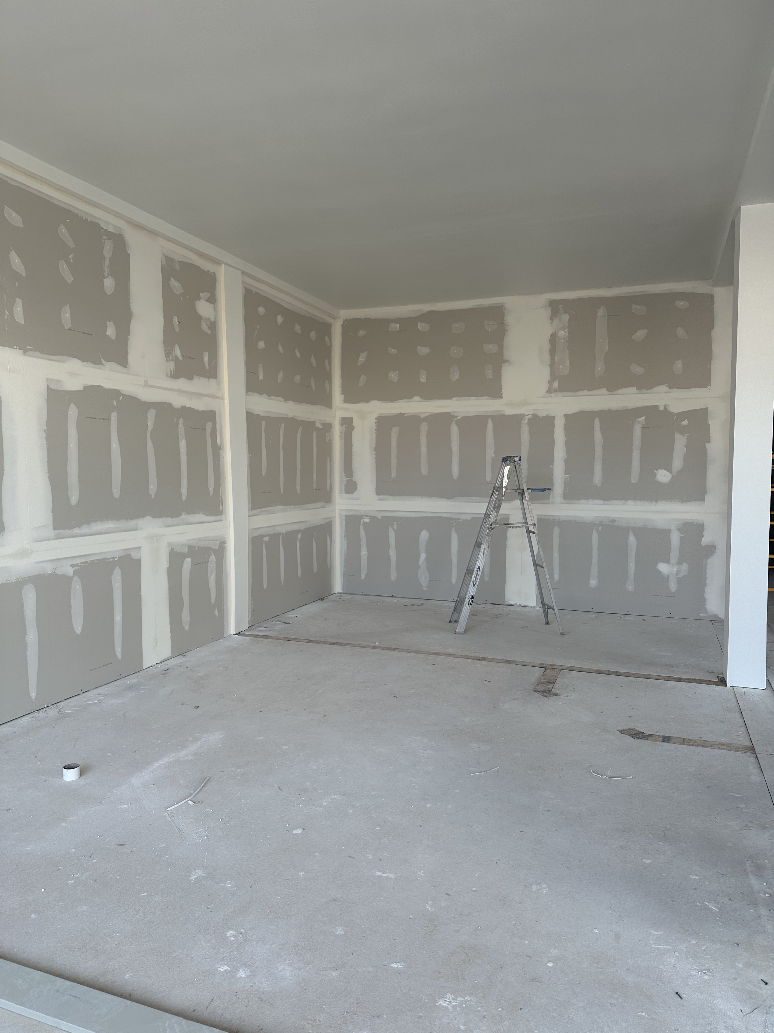 Unfinished room with drywall and a metal ladder in the center, construction materials on the floor.