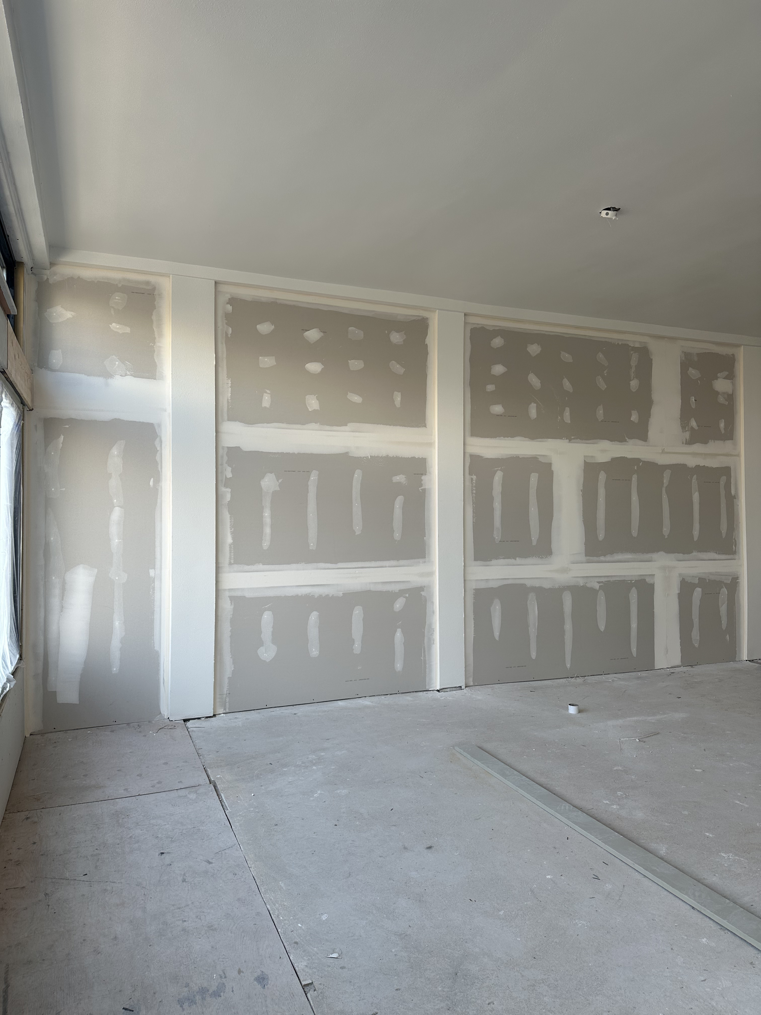 Interior room under construction with drywall installation and unfinished flooring.