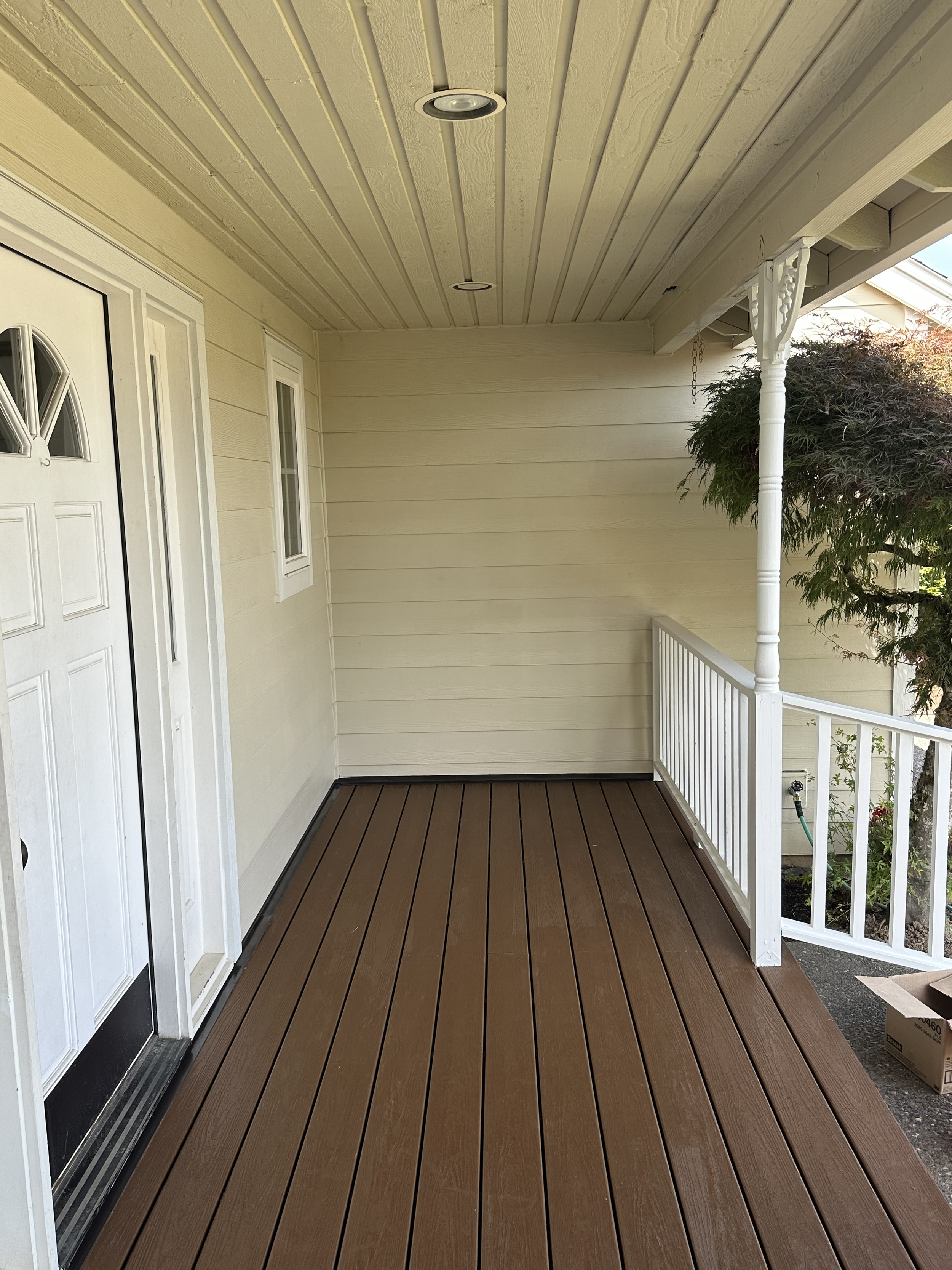 View of a porch with wooden flooring, white walls, a white railing on the right, and a ceiling with recessed lighting.