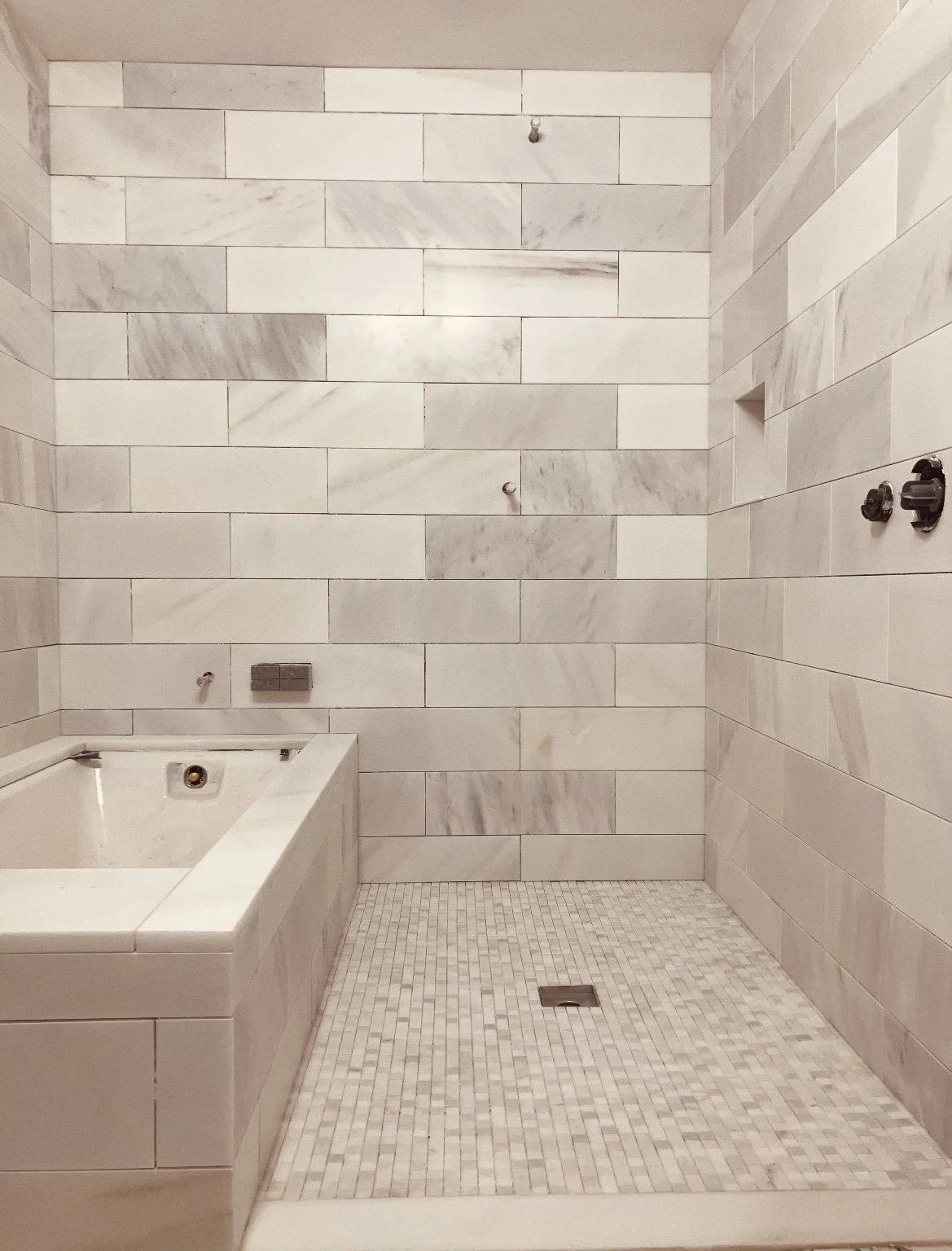 Empty walk-in shower with beige marble tiles, a built-in bathtub, and a tiled floor.