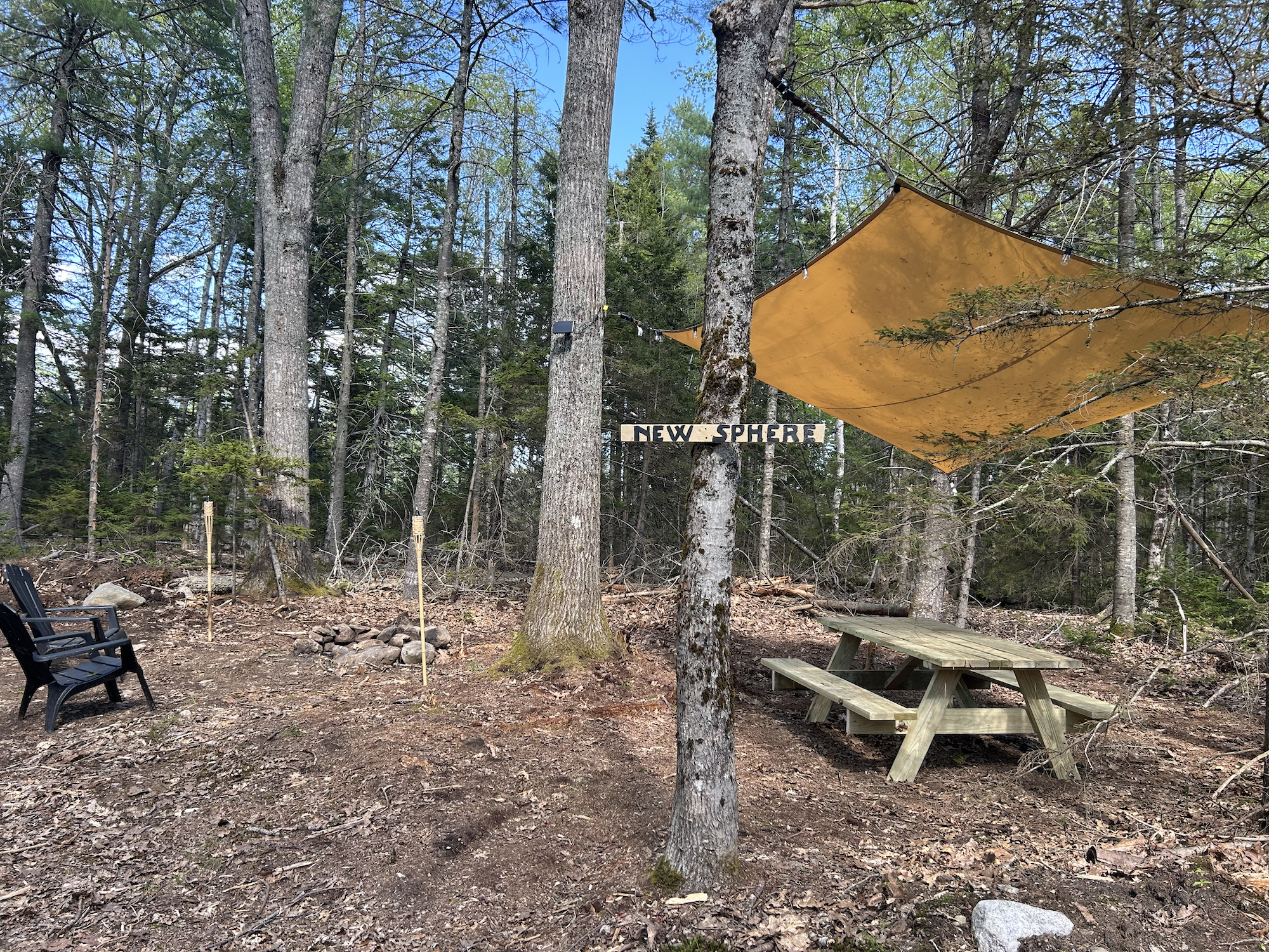 The site includes a sun shade, picnic table, 2 adirondack chairs, a fire pit and solar string lights.