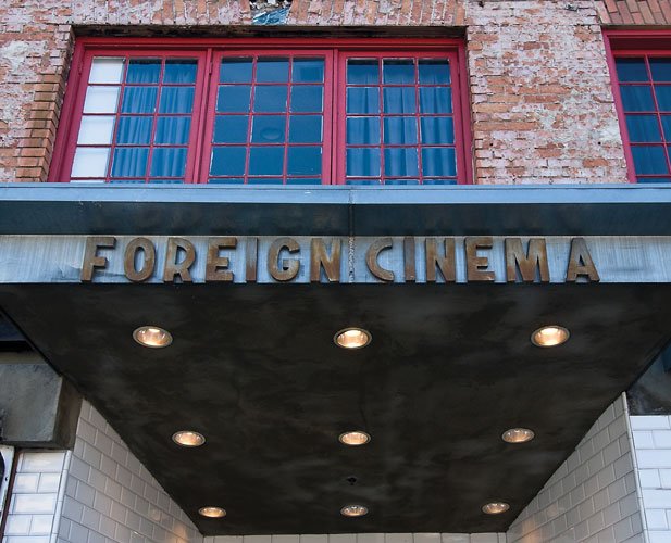 Sign that reads "Foreign Cinema" under red-framed windows and brick building facade.