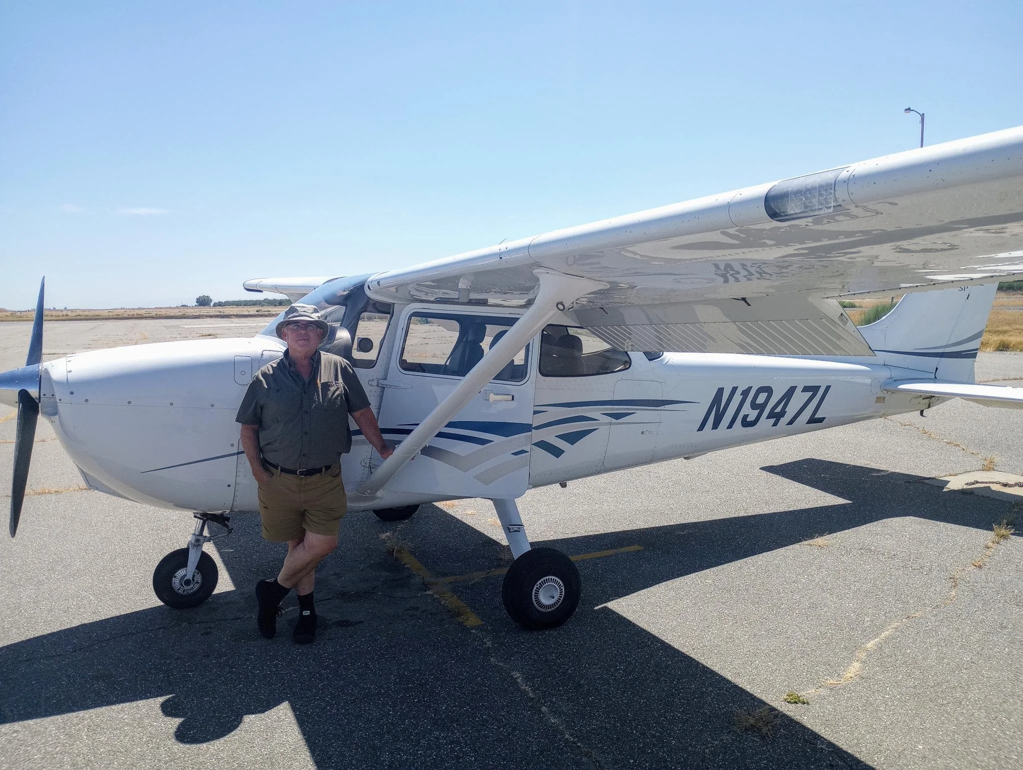 A man standing next to a small white airplane on an empty airstrip on a sunny day.
